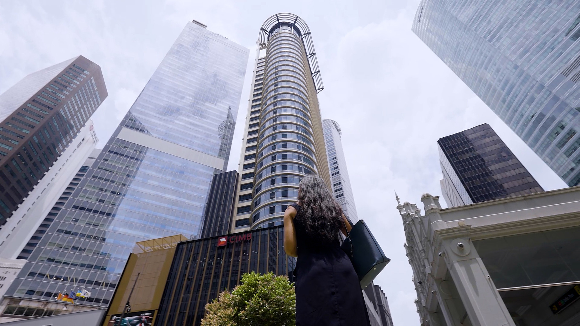 Frau mit Aktenmappe blickt inmitten moderner Hochhäuser in einer urbanen Skyline nach oben.